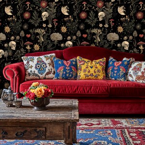 May include: A red velvet sofa with a variety of colorful throw pillows, featuring a skull and floral pattern. The sofa is in front of a black and gold wallpaper with a skull and floral pattern.
