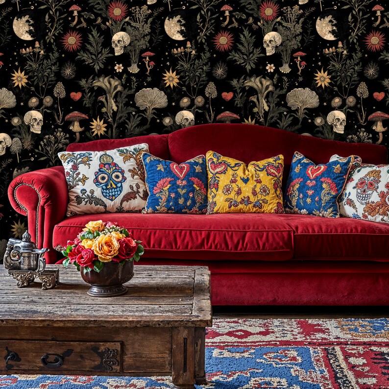May include: A red velvet sofa with a variety of colorful throw pillows, featuring a skull and floral pattern. The sofa is in front of a black and gold wallpaper with a skull and floral pattern.