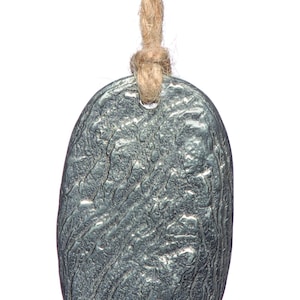 May include: A textured, oval silver pendant suspended from a natural-coloured rope. The pendant has a rough, uneven surface. The rope is knotted at the top of the pendant.