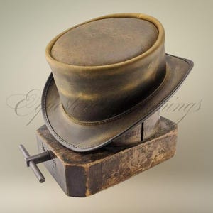 May include: A brown leather top hat with a rounded crown and a wide brim. The hat is displayed on a wooden hat block. The hat has a distressed, vintage appearance.