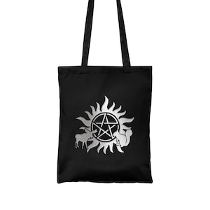 May include: Black tote bag featuring a silver metallic print of a pentagram within a sunburst, accompanied by a moose and a squirrel.