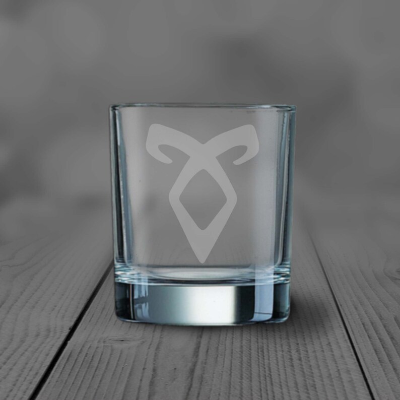 May include: A clear glass shot glass with a white etched design of the rune symbol from the book series "The Mortal Instruments".