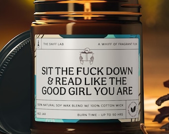 May include: A brown glass jar candle with a black lid, resting on a wooden surface. The label reads "SIT THE FUCK DOWN & READ LIKE THE GOOD GIRL YOU ARE." The candle is made with natural soy wax and a cotton wick, with a burn time of up to 50 hours.