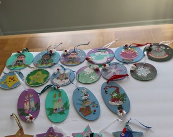 May include: A collection of handmade Christmas ornaments. The ornaments are various shapes, including circles, ovals, and stars. Each ornament is hand-painted with festive designs, such as snowmen, candles, and angels. They are decorated with glitter and small red and white beads.