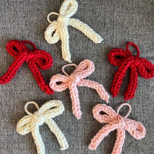 Op de afbeelding: Zes handgebreide strikken in rood, roze en wit. De strikken zijn gemaakt van een dik garen en hebben een eenvoudig, klassiek ontwerp.