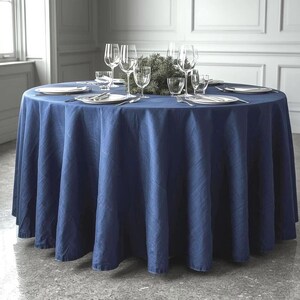 May include: A circular dining table covered with a navy blue tablecloth. The table is set with white plates, cutlery, and wine glasses. A small evergreen centrepiece sits in the middle.