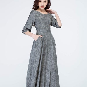 May include: A gray maxi dress with a scoop neck and 3/4 sleeves. The dress has a fitted bodice and a flowing skirt. The sleeves have black trim.