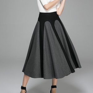 May include: A white short-sleeved top paired with a gray and black skirt. The skirt has a high waist with a black panel and gray panels. The model is wearing black heels.