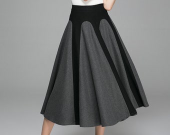 May include: A white short-sleeved top and a grey and black skirt. The skirt has a high waist with a black panel and grey panels. The model is wearing black heels.