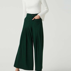 May include: A woman is wearing a white turtleneck sweater and dark green wide-leg trousers with pleats. The trousers have a high waist and pockets.