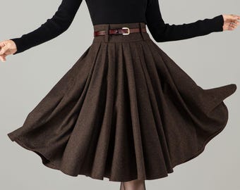 May include: A black long-sleeved sweater paired with a brown pleated skirt and a brown belt. The outfit is completed with brown boots. The skirt has a flared design, and the belt has a gold buckle. The overall style is classic and elegant.
