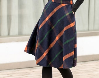 Può includere: Una gonna blu navy con motivo a quadri in arancione e verde. La gonna è lunga fino al ginocchio e ha una silhouette svasata.