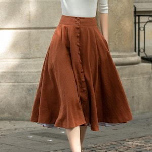May include: A woman wearing a white short-sleeved shirt and a brown midi skirt with a button-up front. She is wearing a straw hat and brown shoes.