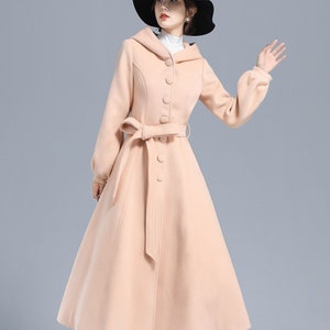 May include: A long, light pink coat with a hood, a belt, and a row of buttons down the front. The coat has a flared skirt and long sleeves.