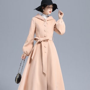 May include: A long, light pink coat with a hood, a belt, and a button closure. The coat has a flared skirt and long sleeves with puffed cuffs.