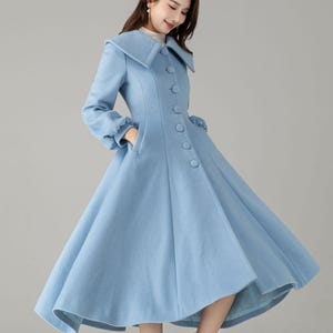 May include: A light blue coat with a large collar and button-down front. The coat has long sleeves with gathered cuffs and a flared skirt. The model is wearing white boots. A stylish, vintage-inspired coat.