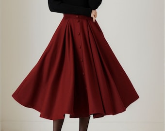 May include: A woman wearing a black long-sleeved sweater and a burgundy midi skirt with a button-up front. The skirt is pleated and has a flared silhouette.