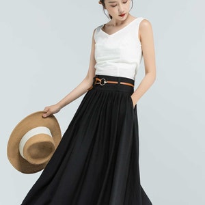 May include: A black maxi skirt with a brown leather belt and a silver buckle. The skirt has pleats and a flowing silhouette.