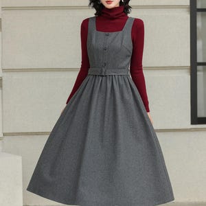 May include: A gray, button-down dress with a belted waist and a flared skirt. The dress is worn over a long-sleeved burgundy turtleneck. The outfit is completed with brown ankle boots.