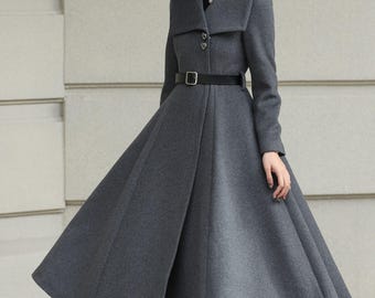 May include: A gray wool coat with a wide, flared skirt and a black belt cinching the waist. The coat features a large collar and is paired with a black hat and boots. The coat's design is elegant and tailored.