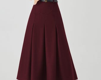May include: A burgundy midi skirt with a high waist and pleats, worn with a black long-sleeved top and a brown belt. The outfit is completed with black tights and heels, creating a classic and elegant look.