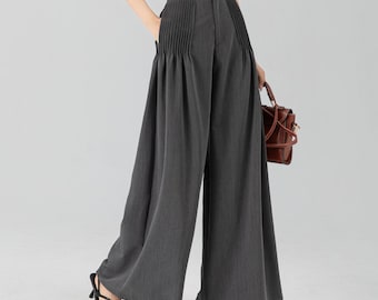 May include: A woman wearing a white short-sleeve top and wide-leg charcoal gray pants. The pants have pleats at the waist. She is also carrying a brown handbag and wearing black heeled sandals.