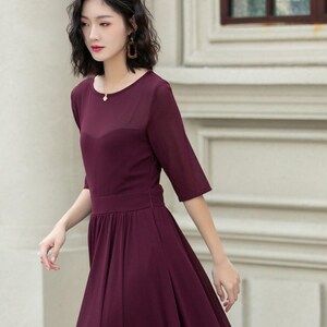 May include: A woman wearing a long, burgundy maxi dress with a round neckline and short sleeves. The dress has a fitted bodice and a flowing skirt. She is wearing black heeled sandals.