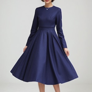 Op de afbeelding: Een marineblauwe jurk met lange mouwen en een uitlopende rok. De jurk heeft een getailleerde taille en een ronde halslijn. Het model draagt ​​hoge hakken. De jurk is een klassieke stijl, geschikt voor formele gelegenheden.