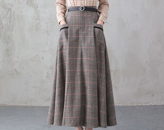 May include: A woman wearing a beige and brown checked long-sleeved shirt with a black belt and a grey and red checked skirt with pockets.