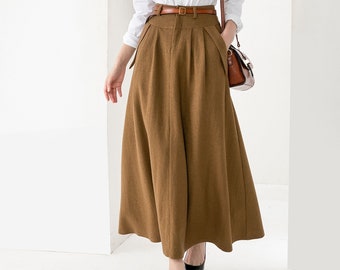 May include: A woman wearing a white long-sleeved button-down shirt with a brown leather belt and a brown maxi skirt. She is carrying a brown leather handbag.