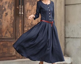 May include: A navy blue dress with long sleeves and a round neckline. The dress features a row of buttons down the front and a red belt cinching the waist. The skirt is pleated and flows to mid-calf length.