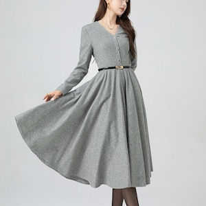 May include: A gray midi dress with a v-neckline and long sleeves. The dress has a button-up front and a black belt with a gold buckle.