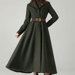 May include: A dark green, long coat with a flared skirt and a brown belt. The coat has a button-down front and a notched collar. The model is wearing brown boots. The coat is a classic style, suitable for fall or winter.