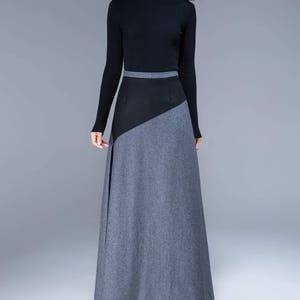 Puede incluir: Una mujer con un suéter negro de cuello alto y una falda larga gris y negra. La falda tiene un diseño geométrico con un panel negro en la parte superior y un panel gris en la parte inferior.
