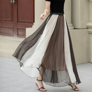 May include: A woman wearing a black top and a white and brown striped maxi skirt. She is wearing a straw hat and holding a white handbag.