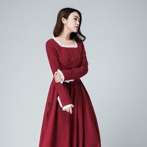 May include: A long-sleeved, burgundy dress with a white lace trim around the neckline and cuffs. The dress has a fitted bodice and a full skirt.