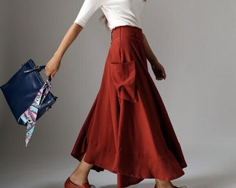 May include: A woman wearing a white top and a long, rust-colored skirt with a large pocket on the side. She is carrying a dark blue handbag with a patterned scarf.