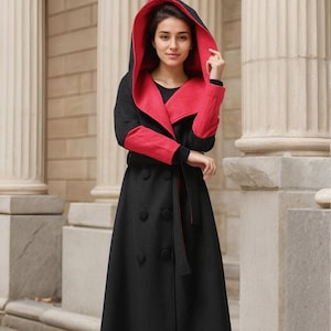 May include: A long black coat with a red hood and red lining. The coat has a belt and a double breasted closure.