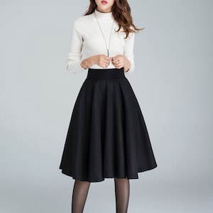 Peut inclure: Une jupe noire &agrave; taille haute avec une silhouette &eacute;vas&eacute;e. La jupe est mi-longue et faite d'un tissu lisse.