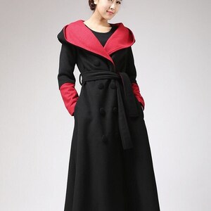 May include: A long black coat with a red hooded collar and a black belt. The coat has a double-breasted closure and two pockets.