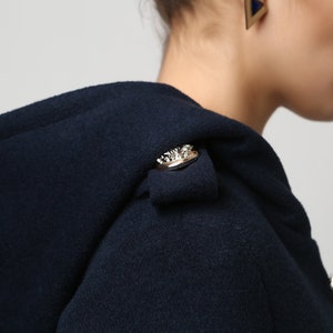 Op de afbeelding: Een donkerblauwe capuchonjas met een gouden knoop op de schouder en een gouden knoop aan de voorkant.