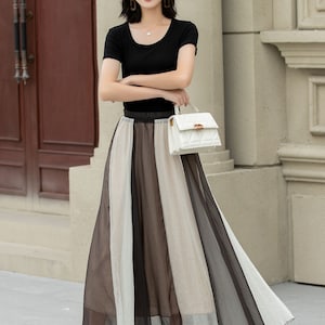 May include: A woman wearing a black short-sleeved shirt, a white hat, a white handbag, and a black and white striped maxi skirt.