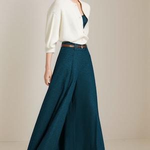 May include: A woman wearing a white cardigan, a teal wide-leg pant, and black heels. The pants have a brown belt.
