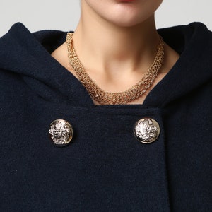 Op de afbeelding: Een donkerblauwe capuchonjas met gouden knopen. De knopen hebben een decoratief ontwerp met een zilveren midden.
