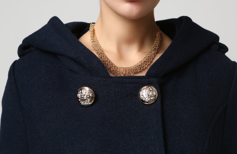 Op de afbeelding: Een donkerblauwe capuchonjas met gouden knopen. De knopen hebben een decoratief ontwerp met een zilveren midden.
