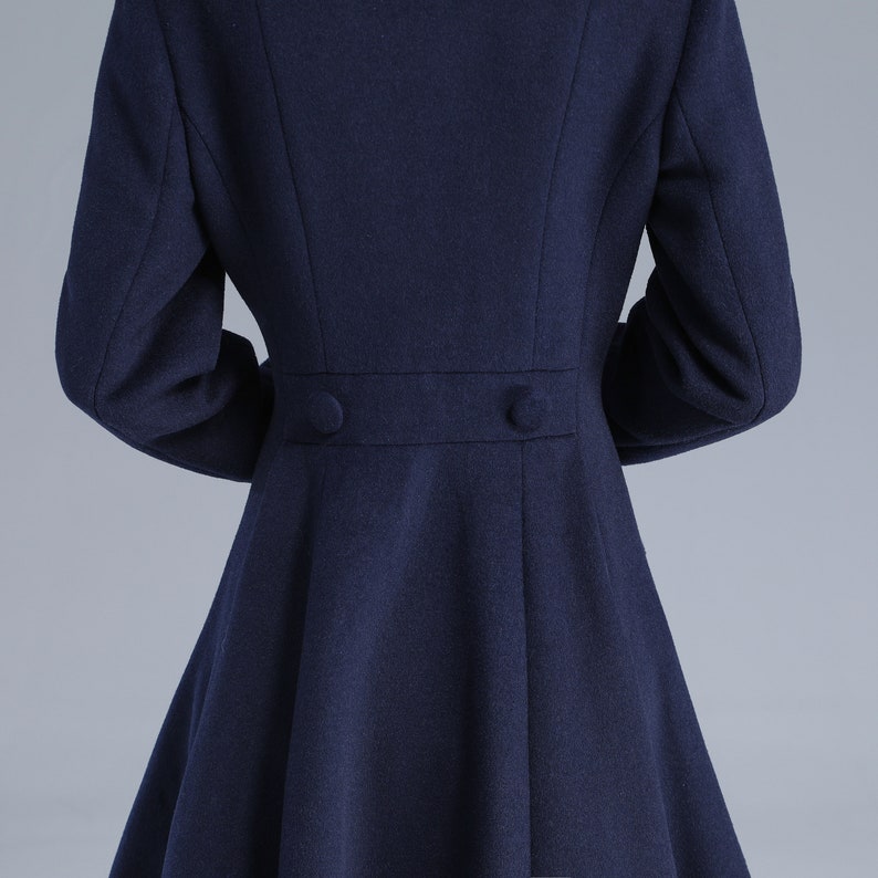 May include: A navy blue coat with a fitted waist and a flared skirt. The coat has two buttons on the back.
