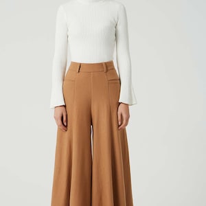 May include: A woman is wearing a white turtleneck sweater and brown wide-leg pants. The pants have a high waist and a wide, flowing leg.