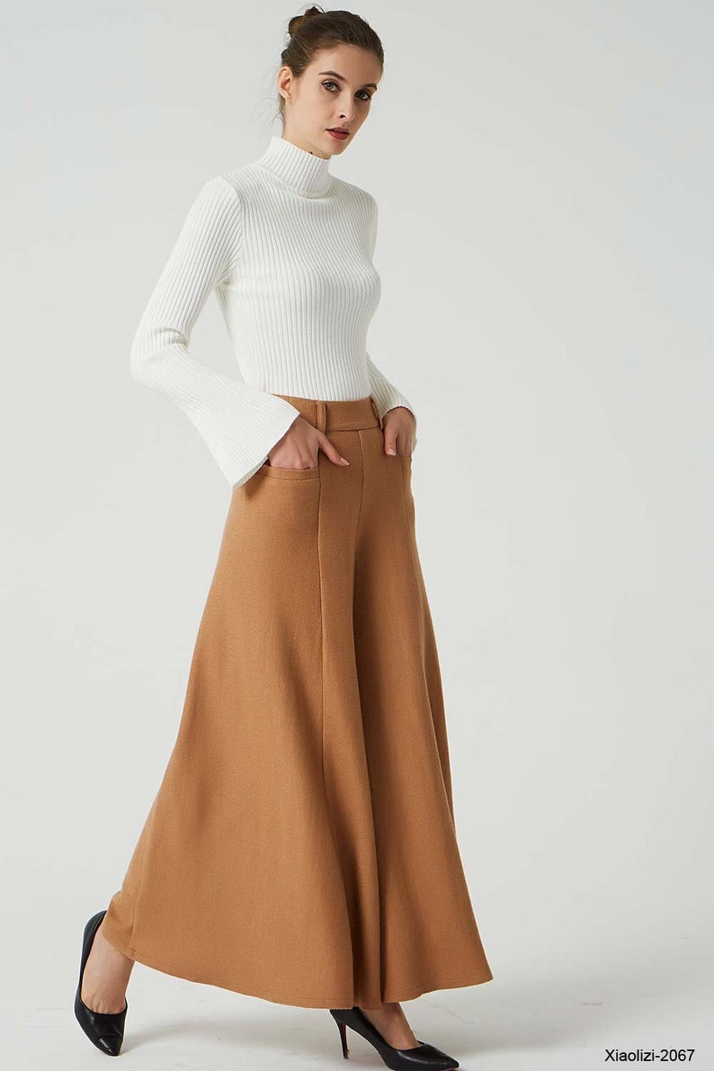 May include: A woman is wearing a white turtleneck sweater with long sleeves and wide bell bottoms. She is also wearing brown wide-leg pants with pockets.