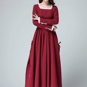 May include: A long, red dress with white lace trim around the neckline and sleeves. The dress has a fitted bodice and a full skirt. The model is wearing black heels.