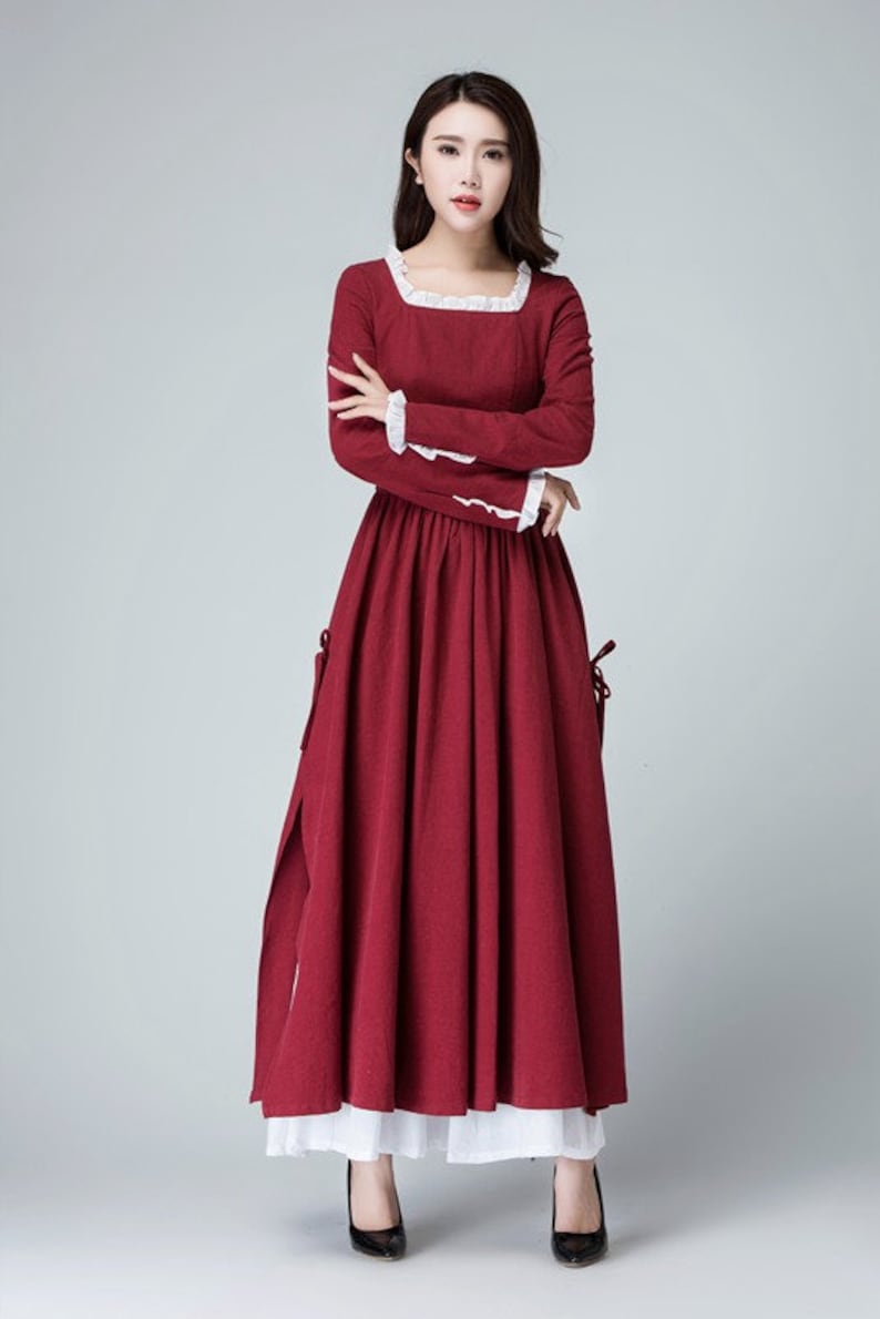 May include: A long, red dress with white lace trim around the neckline and sleeves. The dress has a fitted bodice and a full skirt. The model is wearing black heels.